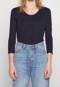 Mörkblå långärmad topp med rund halsringning, kombinerat med högmidjade ljusblå denimjeans med subtil blekning och fem fickor.