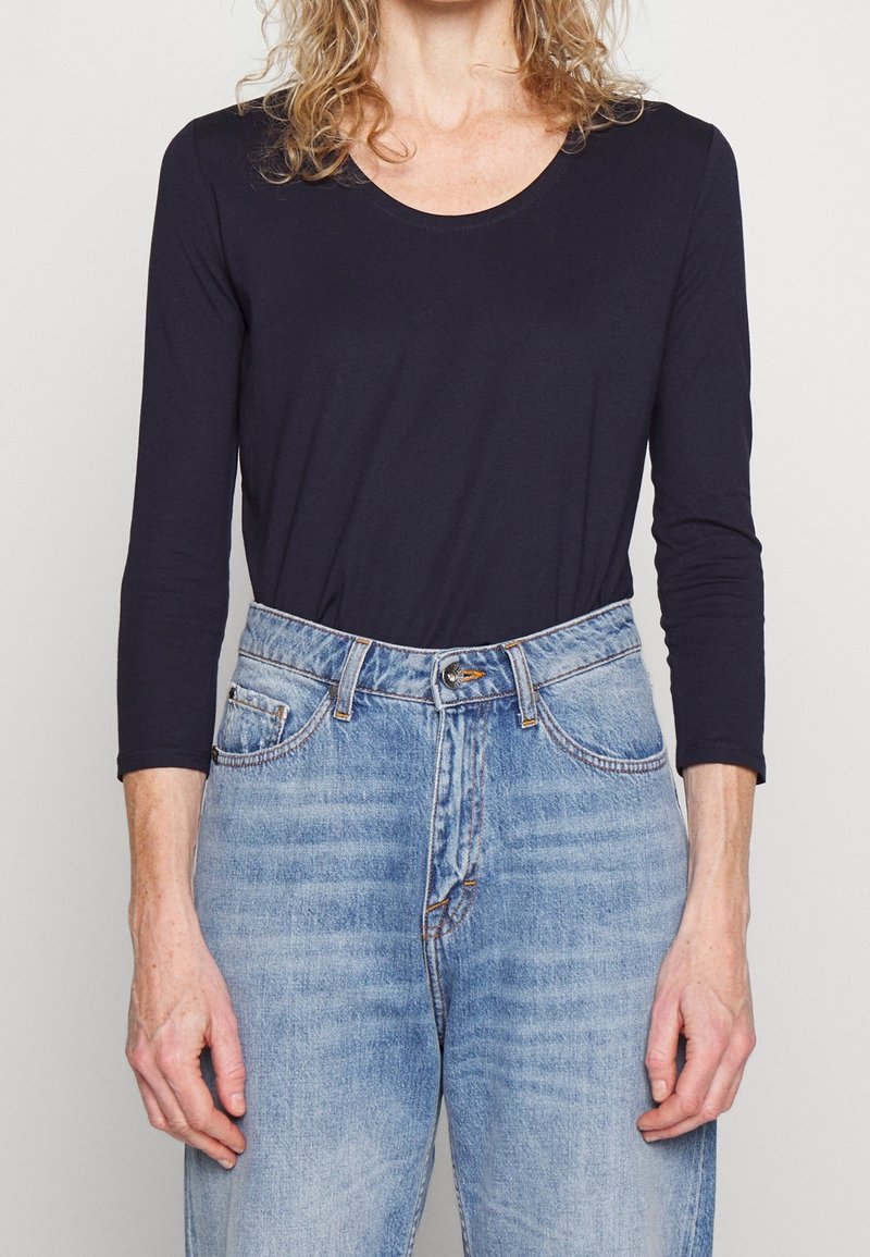 Mörkblå långärmad topp med rund halsringning, kombinerat med högmidjade ljusblå denimjeans med subtil blekning och fem fickor.