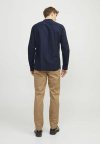 Camicia a maniche lunghe blu navy con colletto a camicia, abbinata a pantaloni khaki. La camicia ha una linea dritta e dettagli di cucitura visibili.