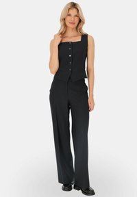 Czarny garnitur w paski, składający się z topu na ramiączkach o kwadratowym dekolcie z guzikami oraz spodni o szerokich nogawkach, wykonany z gładkiego materiału.
