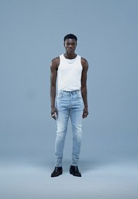 Fehér trikó, világoskék farmer, fekete bokacsizma. A farmer kopott hatású, a modell ezüst láncot és gyűrűket visel.