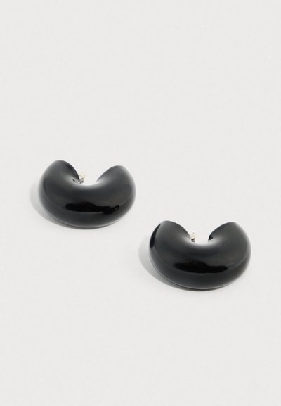 Σκουλαρίκια κρίκοι από μαύρη ρητίνη με γυαλιστερό φινίρισμα, κυρτό σχήμα και μεταλλικά στοιχεία σε ασημένιο χρώμα. Διαμέτρου περίπου 5 εκατοστών.