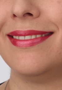 Close-up van lippen met felroze lippenstift met een gladde textuur, waarbij rechte, witte tanden en zachte huidtinten in de omgeving zichtbaar zijn.