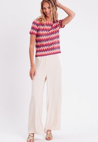 Haut à manches courtes à motif zigzag coloré associé à un pantalon large beige doux. La tenue est complétée par des sandales dorées à lanières.