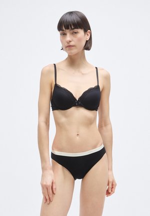 Reggiseno imbottito nero con rifiniture in pizzo, spalline regolabili e un piccolo fiocco. Mutandine nere in cotone con elastico in vita beige a contrasto.
