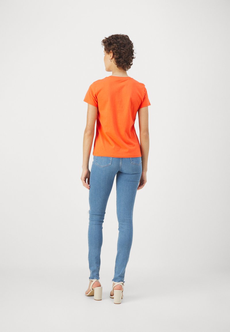 Oranges T-Shirt mit kurzen Ärmeln, kombiniert mit hellblauen Skinny-Jeans. Das Shirt hat einen Kragen und die Jeans verfügen über einen verwaschenen Saum.