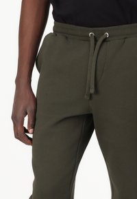 Olive green sweatpants featuring an elastic waistband with drawstring, side pockets, and soft, smooth fabric texture.