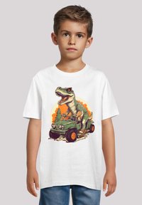 White short-sleeve t-shirt featuring an illustration of a dinosaur driving a green jeep, set against an orange sunset background.
