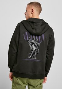 Sudadera negra con un gráfico detallado de un ángel en gris y texto morado, además de puños y dobladillo acanalados. Ajuste casual y cómodo.