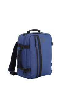 Mochila de tela azul que presenta un bolsillo frontal con cremallera, correas ajustables y un asa en la parte superior para mayor comodidad al llevar. Incluye hebillas laterales.