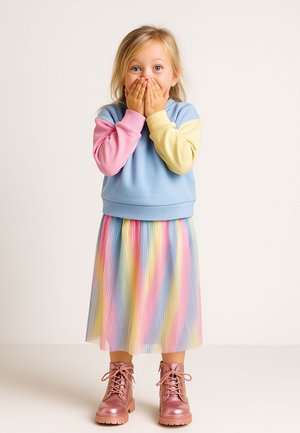 Ein farbenfrohes Kleid mit einem blauen Oberteil und rosa sowie gelben Ärmeln, kombiniert mit einem plissierten, gestreiften Rock in Pastellfarben und glänzenden rosa Stiefeln.
