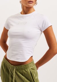 Valge lühikeste varrukatega crop top, millel on hõbedane skriptilogo "Juicy". Sile puuvillane materjal, ümara kaelusega ja külgmised lõhikud.