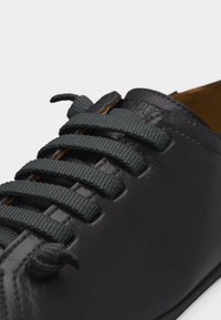 Chaussure en cuir noir avec lacets élastiques tissés gris foncé sans nouer, gros plan montrant les détails de la texture et des coutures.