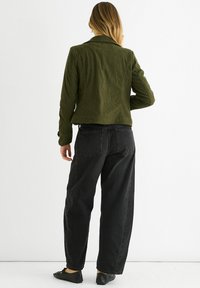 Olive green corduroy jacket with a structured collar, buttoned cuffs, and a slightly cropped fit, paired with black baggy jeans.