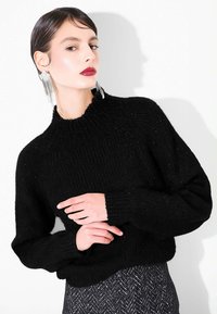 Maglione nero a coste con collo alto e vestibilità relax, abbinato a una gonna grigia a fantasia pied de poule testurizzata. Orecchini argento di grande impatto.