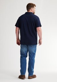 Navyblauwe polo met korte mouwen, gemaakt van katoen, rechte snit. Gecombineerd met lichtblauwe denim jeans en bruine schoenen.