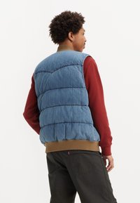 Denim puffer prsluk, svijetloplave boje s kvadratnim dijelovima, uparen s burgundskom dugom majicom i tamnim hlačama, s rebrastim rubom.