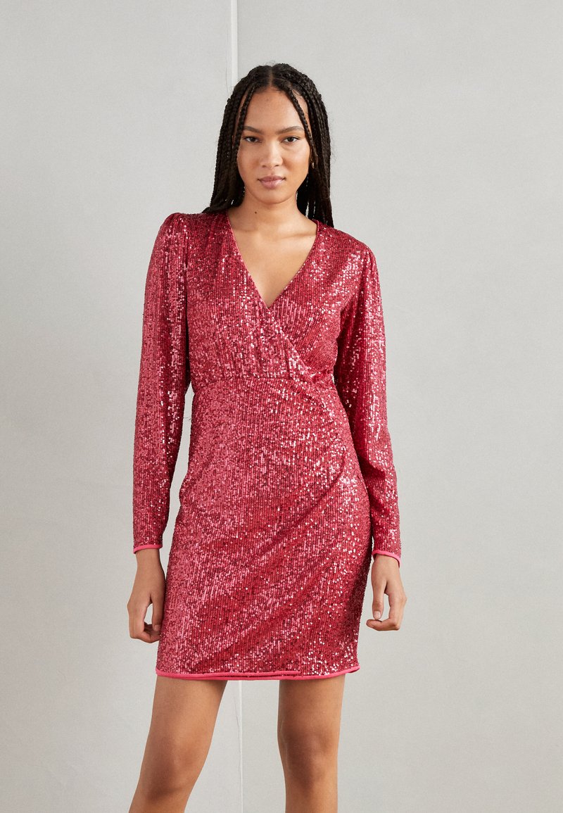Robe rouge à sequins avec des manches longues, un décolleté en V profond et un design croisé. La jupe met en valeur une silhouette ajustée, une texture scintillante et une bordure rose.