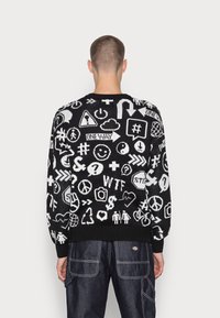 Maglione nero a maglia con simboli grafici e testo bianchi, colletto e polsini a coste, e vestibilità casual.