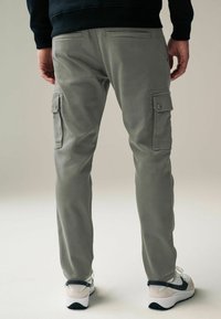 Helle graue Cargo-Shorts mit Seitentaschen, schmaler Schnitt und glatter Baumwolloberfläche, kombiniert mit weißen Sportschuhen mit dunklen Akzenten.