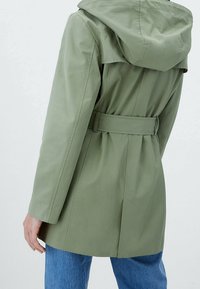 Olive green, lightweight raincoat with a hood, belted waist, and back vent detail. Smooth texture and minimal seams enhance functionality.
