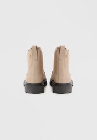 Stivaletti alla caviglia in suede beige con una superficie liscia, linguette sul retro e una robusta suola in gomma nera. Design semplice con dettagli minimi.
