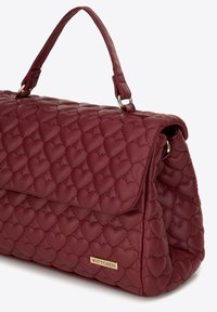 Burgundská prošívaná kabelka s motivem srdce, hladkým povrchem, horním uchopem a zlatým akcentem loga značky.