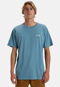 Lysblå bomulds T-shirt med rund hals, korte ærmer og et lille hvidt logo på venstre bryst. Lige skåret nederste kant.
