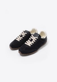Zapatillas de ante azul marino con cordones color crema, costura texturizada y suela de goma. Incluye un parche con el logotipo en la lengüeta y un acento en el talón con un patrón.