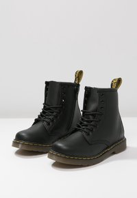 Bottines montantes en cuir noir à lacets avec fermetures éclair latérales, coutures jaunes et languettes de tirage griffées à l'arrière.