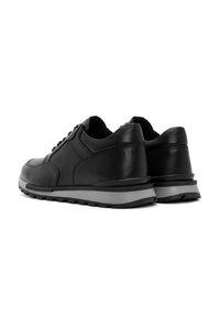 Un paio di sneaker nere in pelle con suole grigie, viste da un lato posteriore su uno sfondo bianco.