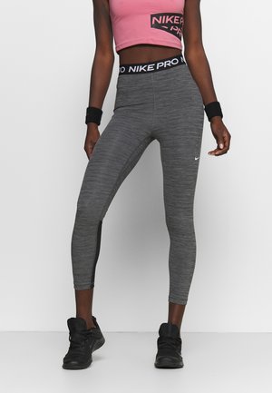 Leggings de sport gris avec un design ajusté, tissu texturé et un bandeau noir Nike Pro. Associés à un haut court rose et des baskets noires.