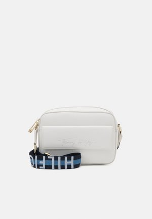 Hvid rektangulær crossbody taske med frontlomme, guldfarvet hardware og en aftagelig sort-og-blå rem med hvid "HILFIGER" tekst.
