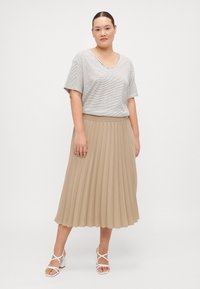 Stripet, kortermet topp i svart og hvitt, kombinert med en plissert, beige midiskjørt. Outfiten fullføres med hvite sandaler med remmer og høye hæler.