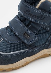 Zapatilla de caña alta en azul oscuro con materiales de malla texturizada y ante, que incluye una correa de Velcro, costuras en contraste y una suela de goma.