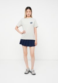 Tricou din bumbac gri deschis cu imprimeu grafic, asortat cu o fustă plisată de culoare albastru închis. Tinuta include încălțăminte slip-on gri.