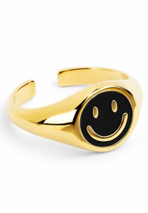 Bague anneau ouverte en or avec un visage circulaire noir présentant un motif smiley en or en relief.