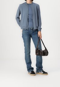 Ljusblå bomberjacka, matchande T-shirt, klassiska blå jeans och svarta sneakers med vita ränder. Brunt handtag med framfickor.