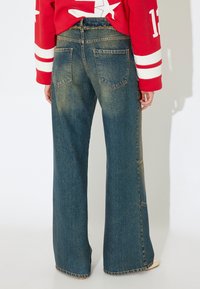 Pantalones vaqueros de pierna ancha en un tono azul oscuro, con una cintura alta, grandes bolsillos traseros y un dobladillo sin terminar con sutiles desgastes y detalles de costura.