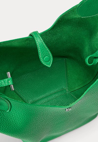 Zaļas ādas rokassomas atvērums, kas rāda teksturētu iekšpusi, mazu izšūtu maisiņu un sānos esošu sprādzīti.