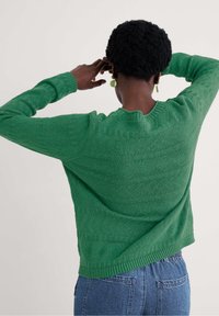 Zaļš adīts džemperis ar faktūru un zigzaga rakstu, apaļu kakla izgriezumu, kā arī ribota apmale un piedurknes. Nēsāts ar augstiem jostas bikšu.