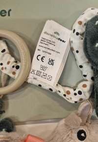 Silicone teether with a fabric loop featuring a polka dot pattern in earthy tones. Label with care instructions and branding is visible.