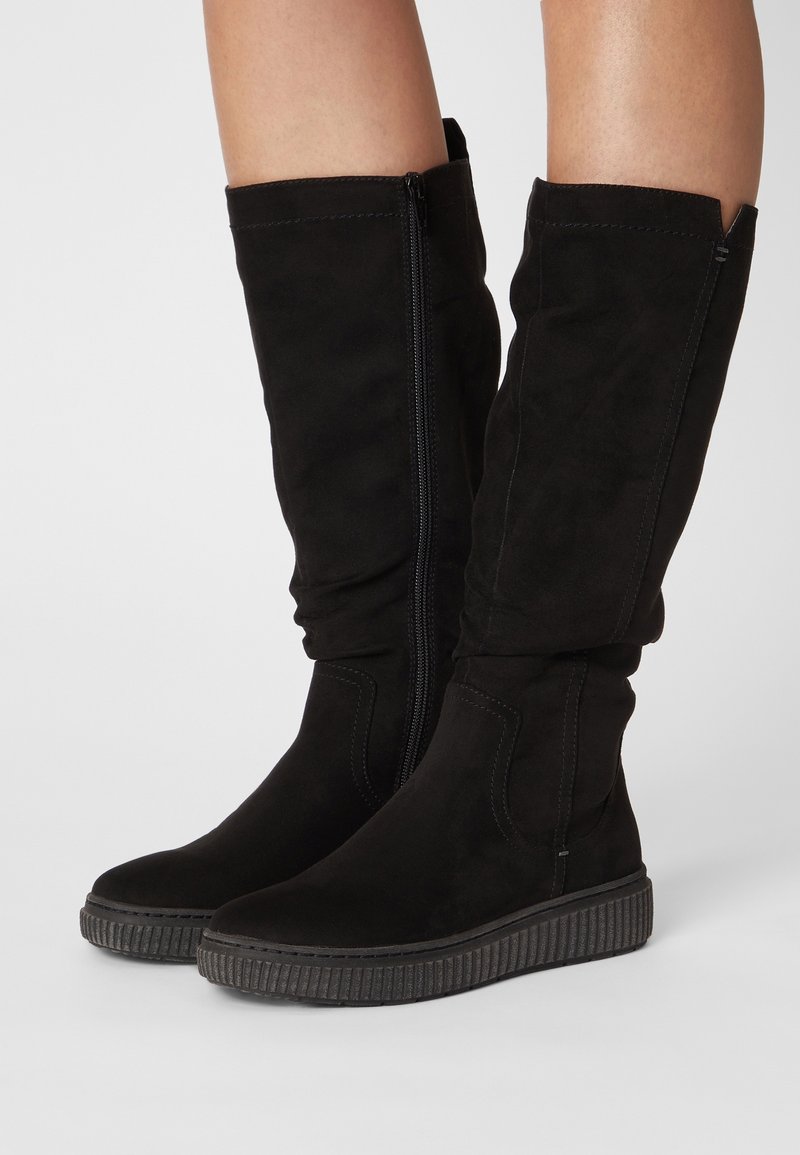 Bottes montantes en daim noir avec une semelle en caoutchouc texturée, fermeture éclair et tige froncée pour un ajustement décontracté. Détails de couture minimalistes visibles.