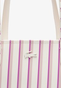 Bolso de mano texturizado en blanco con rayas verticales en rosa y púrpura. Presenta un pequeño logo blanco en forma de cocodrilo.