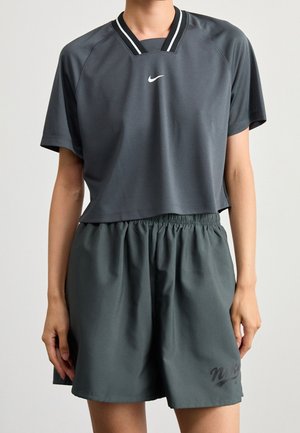 Osoba ubrana w ciemnoszary krótki sportowy shirt Nike z krótkimi rękawami i dopasowane elastyczne szorty z wysokim stanem na jednolitym tle.