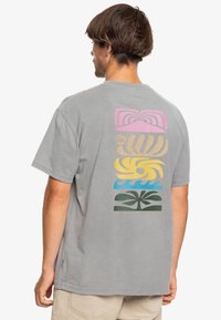 Gray t-shirt featuring a multicolored graphic design on the back with abstract shapes in pink, yellow, blue, and green. Short sleeves, relaxed fit.