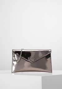 Pochette argentée métallique avec fermeture à rabat, bandoulière en chaîne et logo en accent. Présente une texture lisse et réfléchissante ainsi qu'une forme rectangulaire.