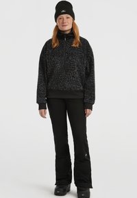Mustat fleece-pullot, joissa on vetoketjukaulus ja huomaamaton teksturoitu kuvio, yhdistettyinä mustiin slim fit -housuihin ja mustiin lumikenkiin.