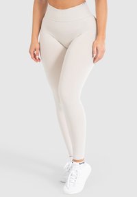Leggings a vita alta di colore crema con una texture liscia e una cintura a costine, indossati con scarpe da ginnastica bianche.
