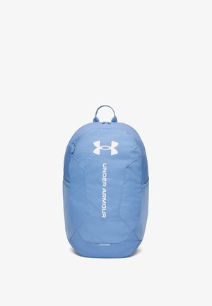 Modrý batoh Under Armour s bielym logom a vertikálnym textom, predný vrecko so zipsom a bočné sieťované vrecká na bielom pozadí.